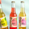 4 flavours of Kombucha on a blue background with 1 being picked up