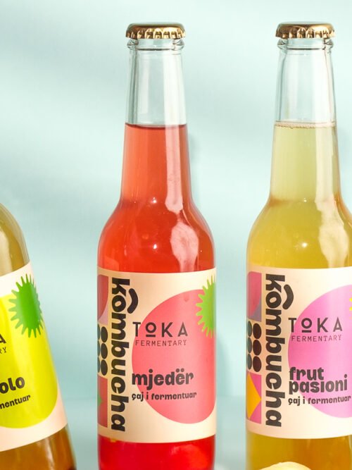 4 flavours of Kombucha on a blue background with 1 being picked up