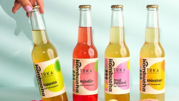 4 flavours of Kombucha on a blue background with 1 being picked up
